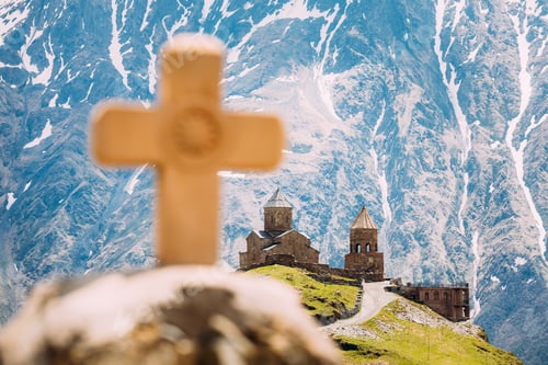 Preview: Stepantsminda, Gergeti, Georgia. Cross On Stones On Mountains Background Near Gergeti Trinity