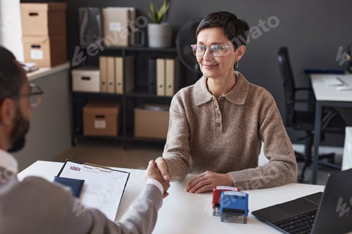 Preview: Happy mature woman shaking hand of male applicant after approving visa