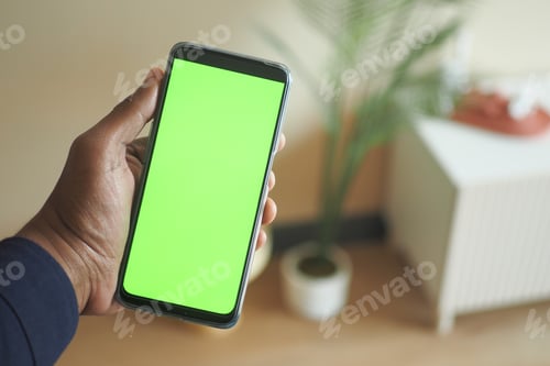 Preview: holding smart phone with green screen and home interior decoration on table