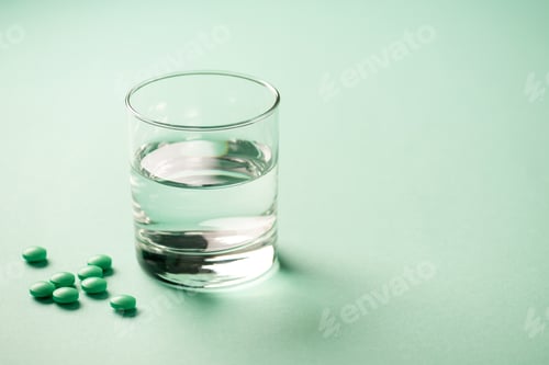 Preview: close-up view of glass of water and medical tablets on green