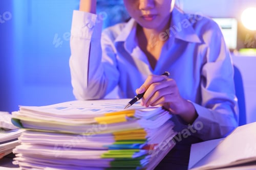Preview: A young woman works overtime night at her desk in office,using laptop reviewing documents.stressed