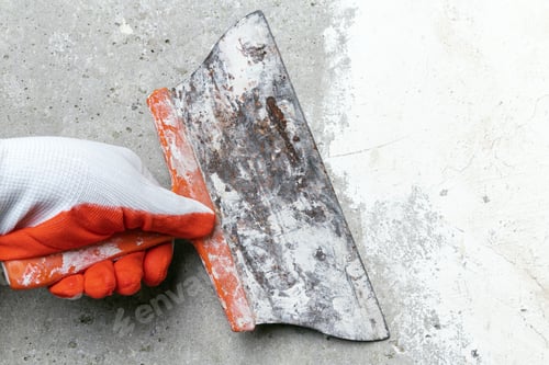 Preview: Hand of plasterer holds old trowel, scrubbing concrete wall, removes old plaster during redecoration