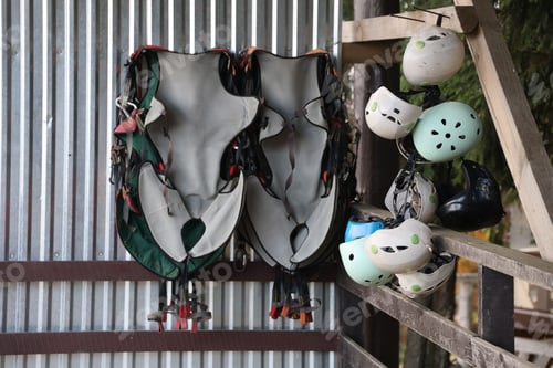 Preview: Climbing equipment - colorful helmets and safety vests hanging on a board in a rope park