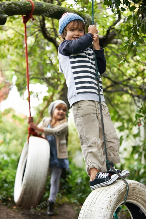 Preview: Swing life away. Shot of two cute kids playing on tire swings in their garden.