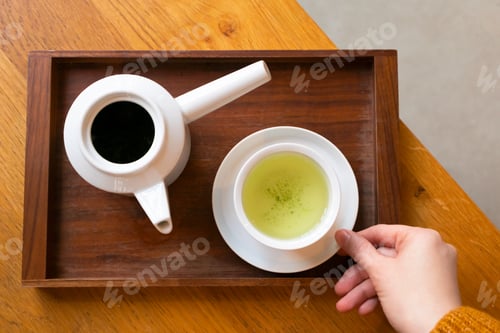 Preview: Woman holding white cup with Japanese green tea and teapot on wooden serving tray on table
