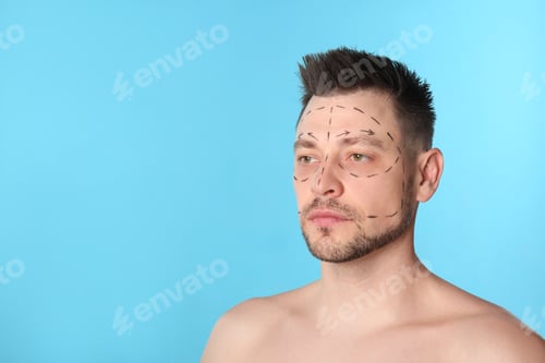 Preview: Man with marks on face for cosmetic surgery operation against blue background. Space for text
