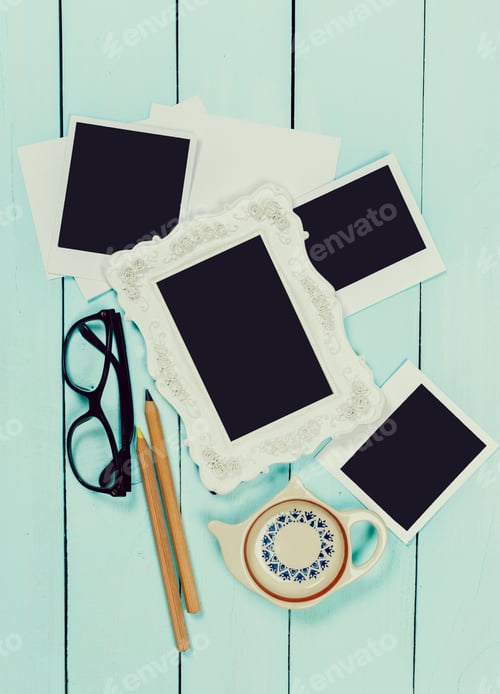Preview: Creative workspace featuring empty frames, stationery, and a teapot on a wooden table