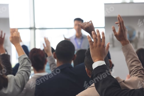 Preview: Rear view of diverse business people raising hands in a business seminar in office building
