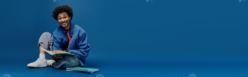 Preview: Young handsome man with a joyful smile sitting comfortably on a blue backdrop