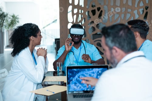 Preview: Diverse male and female doctors wearing face masks sitting at table and using vr glasses