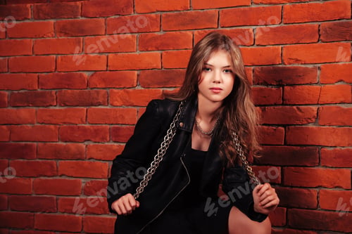Preview: Confident Teenage Girl Poses in Black Leather Jacket Against a Red Brick Wall