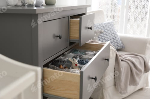 Preview: Modern open chest of drawers with baby clothes and accessories in room, closeup