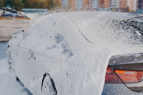 Preview: Car in white soap foam during cleaning with high pressure washer at carwash station