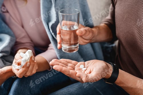 Preview: Close up of middle aged man giving pills his wife, flu concept with tissues and blanket