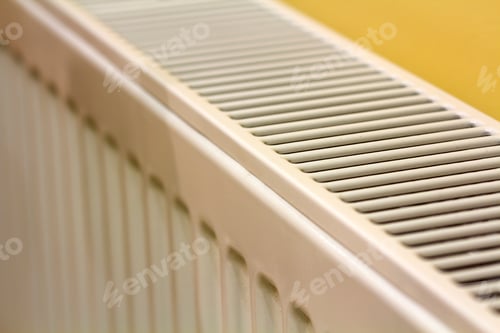 Preview: Close-up of white heating radiator detail on light yellow wall copy space background.