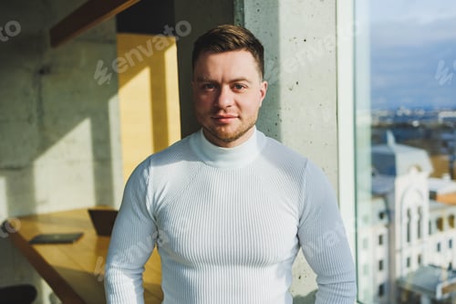 Preview: A young handsome man in a white sweater is standing in a spacious bright office