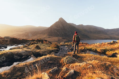 Preview: Man stands atop a majestic mountain peak, looking out onto an expanse of water