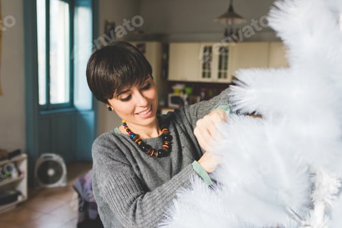 Preview: Young woman at home decorating xmas tree
