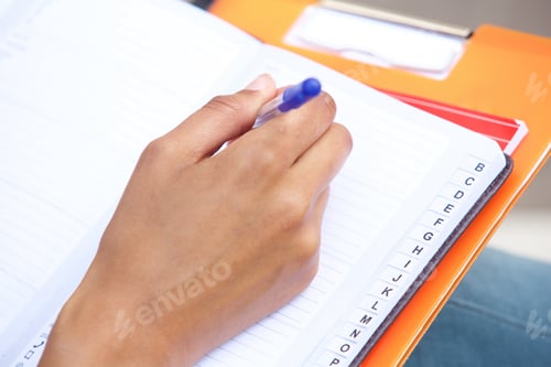 Preview: female hand holding pen and writing in book
