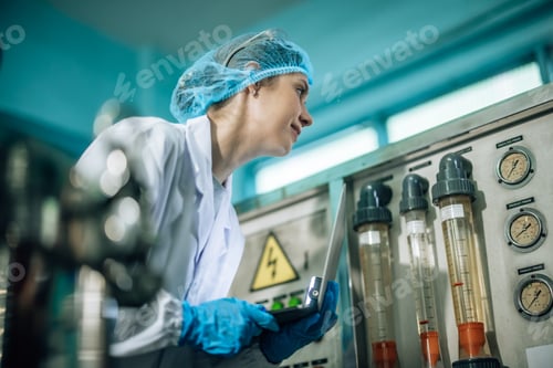 Preview: Woman Inspecting Industrial Equipment with Laptop in Factory