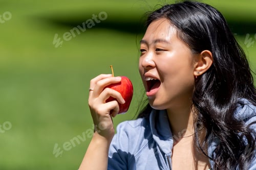 Preview: Asian woman eating a red apple in the park