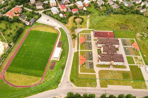 Preview: Aerial view of sports stadium with red running tracks and green grass football field near school