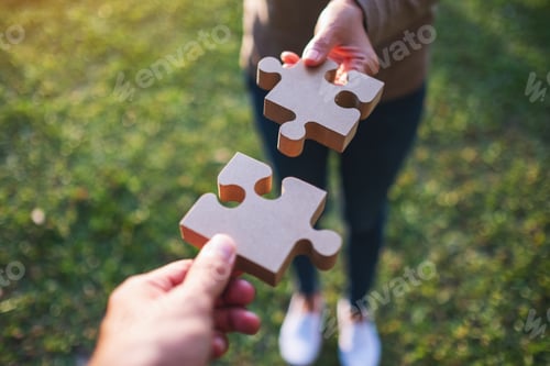 Preview: Closeup image of two people holding and putting a piece of wooden jigsaw puzzle together