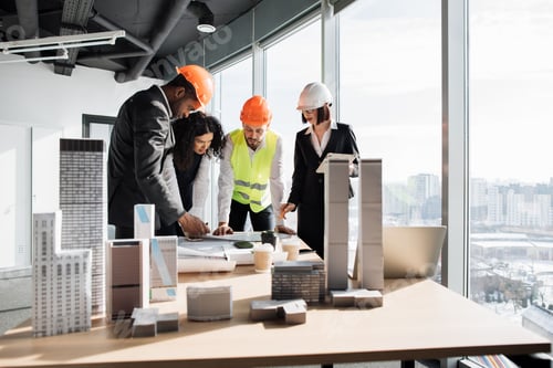 Preview: Multiracial coworkers builders and architects standing near table with blueprints