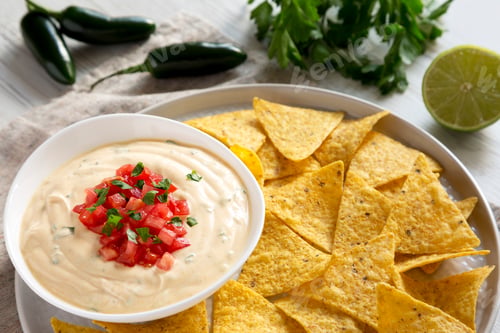 Preview: Homemade cheesy dip in a bowl, yellow tortilla chips over white wooden background, side view.