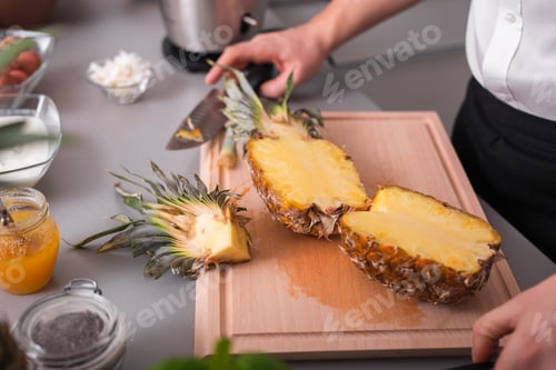Preview: Unrecognizable man cutting a pineapple on chopping board.