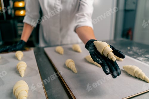 Preview: baker's hands placing shaped uncooked croissants on a baking sheet with parchment baking in the oven