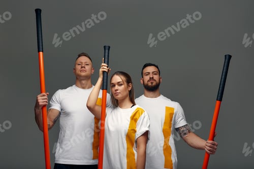 Preview: Two men and woman aikido fighters with wooden fight stick posing in studio, fight demonstration