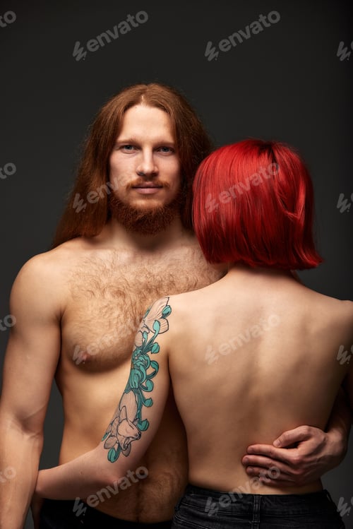 Preview: Sexy half naked couple in love. An attractive man with long hair and a beard looks at the camera, a