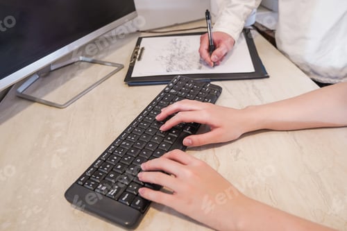 Preview: One person typing on a keyboard, while another takes notes in a folder. Teamwork