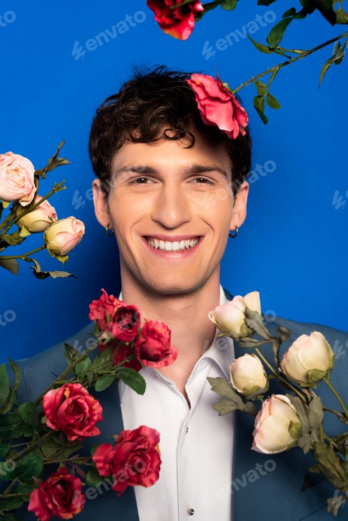 Preview: Portrait of smiling man in elegant clothes looking at camera near flowers on blue background