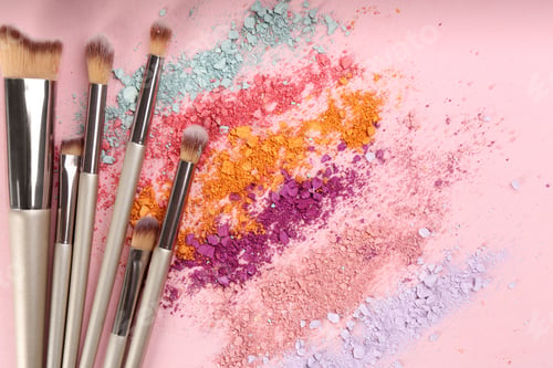 Preview: Makeup brushes and scattered eye shadows on pink background, flat lay