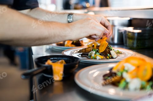 Preview: Cropped image of chef putting final garnish on dish in restaurant