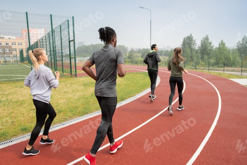 Preview: Rear view of young intercultural people in activewear running down race track