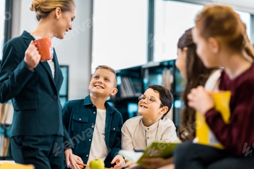 Preview: smiling librarian looking at cute schoolchildren in library