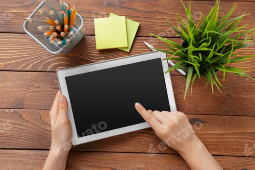 Preview: woman holding blank tablet device over a wooden workspace table