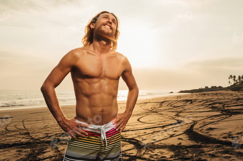 Preview: handsome smiling shirtless man standing on beach during sunset in bali, indonesia