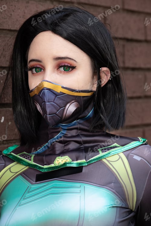 Preview: Female cosplayer in a green action suit against a brick wall