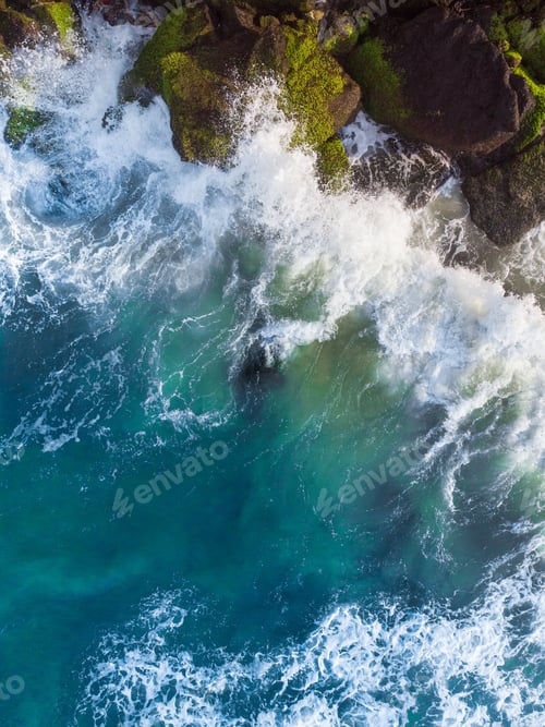 Preview: Vertical overhead aerial shot of a wavy blue sea against the rocks