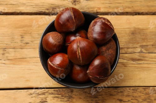 Preview: Fresh edible sweet chestnuts in bowl on wooden table, top view