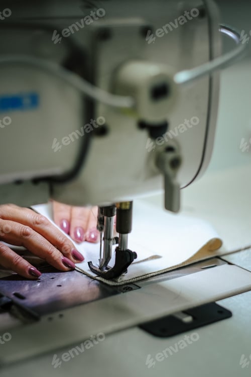 Preview: Vertical closeup shot of female hands operating an industrial sewing machine