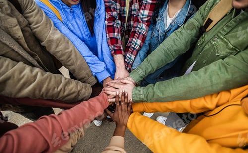 Preview: Diverse group of young friends stacking hands outdoors showing support and unity
