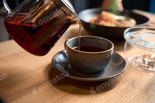 Preview: Close-up view person pouring freshly brewed loosed leaves tea into cup