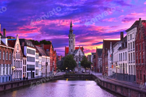Preview: Scenic purple sunset over the houses and the Poortersloge on the bank of a river in Bruges, Belgium