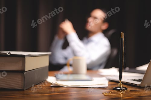 Preview: Closeup of a pen attached to a chain in stand lying on desk near laptop and books with documents