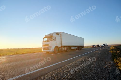 Preview: Semi-truck with cargo trailer driving on highway hauling goods in evening.